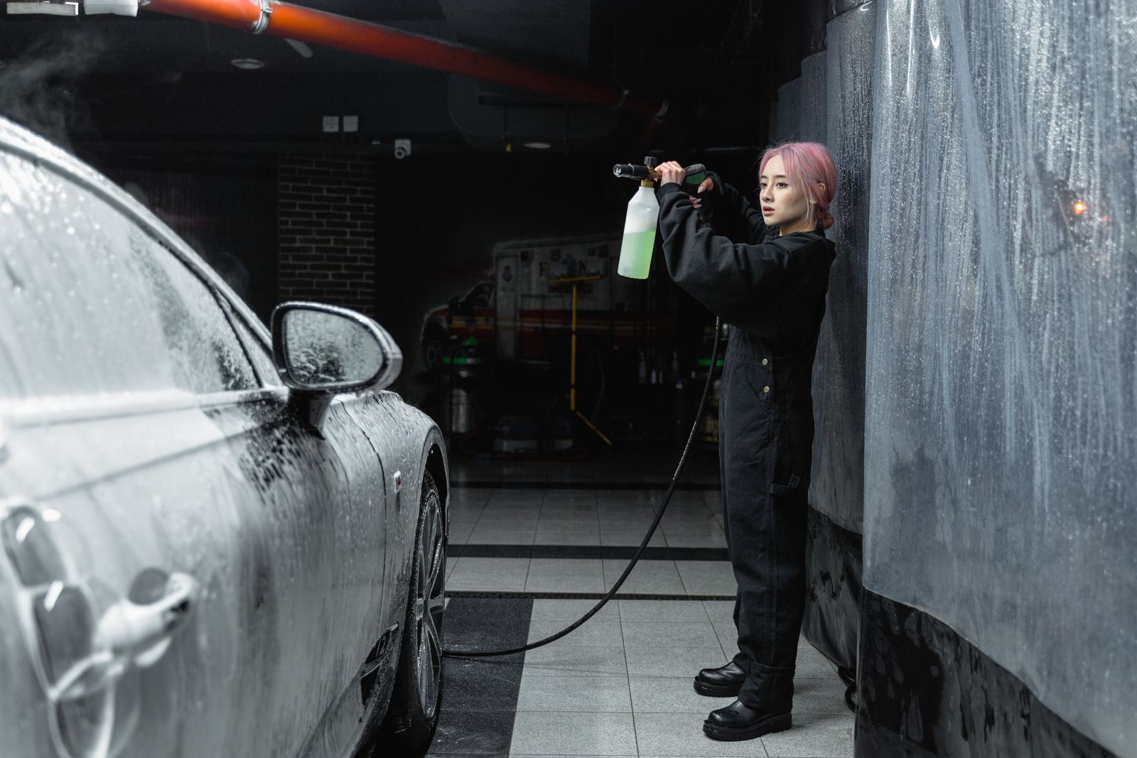 Detailer pre-rinsing a black sedan in the wash bay